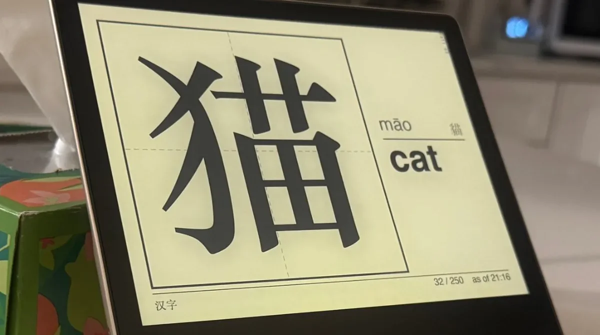 An e-ink flashcard display showing the character 猫 on a kitchen counter